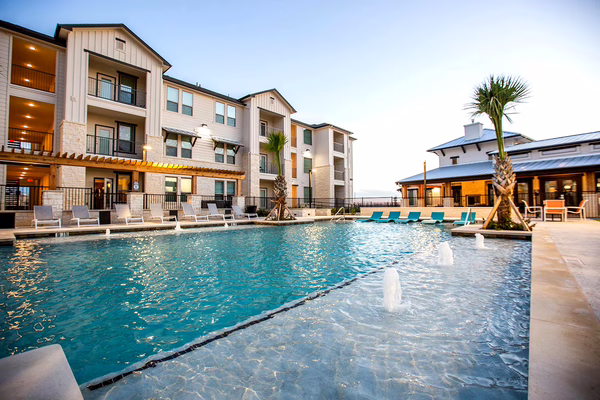 The Flats at Shadowglen multifamily community with resort-style pool, sun shelf, lounge chairs, and clubhouse at sunset